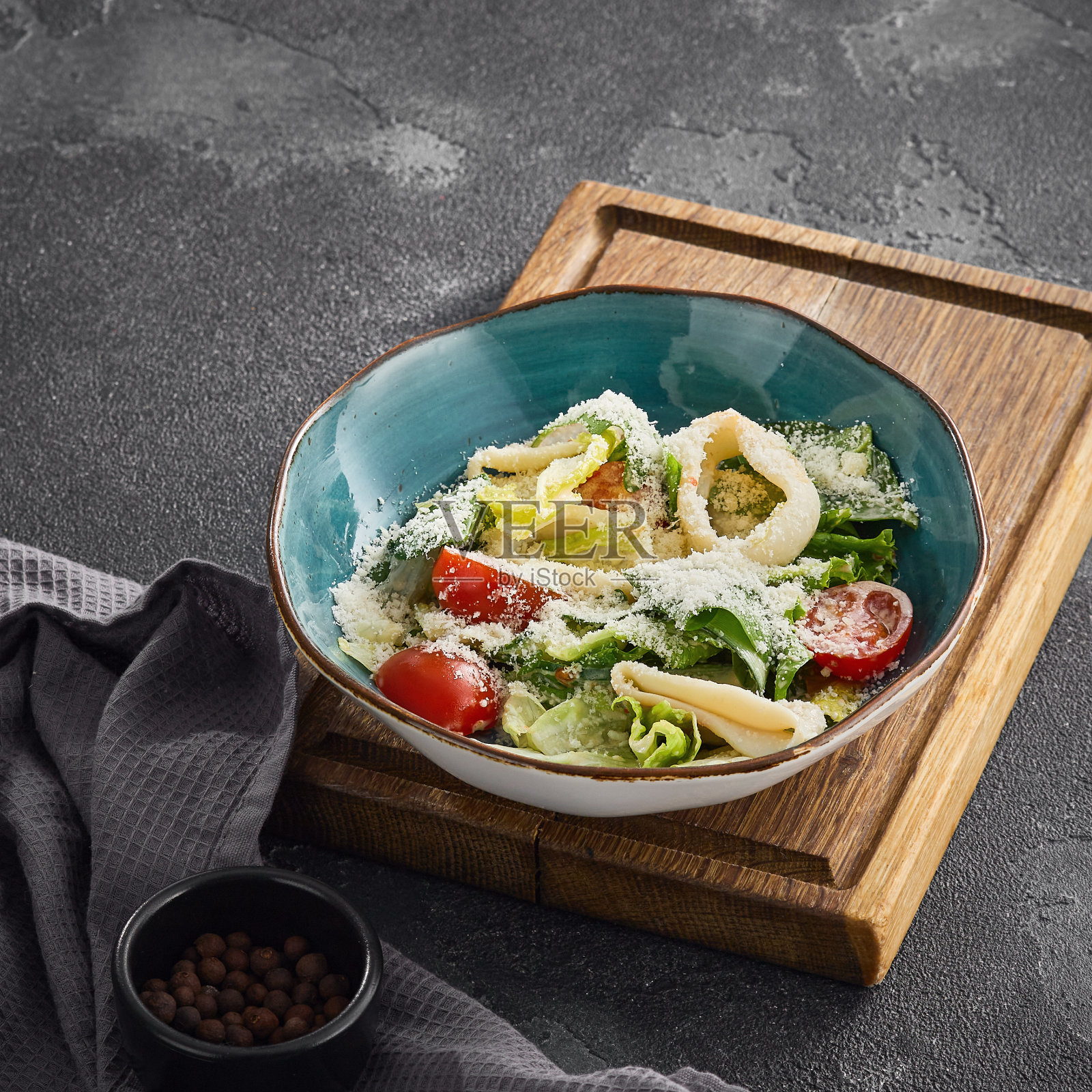 新鲜的混合沙拉，樱桃番茄和鱿鱼在一个木板碗，一个美食家触摸健康的一餐。照片摄影图片