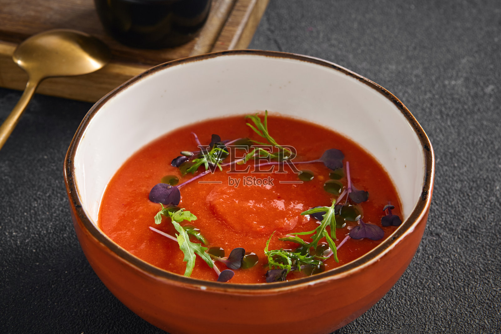 经典的冷西班牙凉菜番茄汤配以新鲜的香草，盛在一个质朴的碗里，表面是黑色的石头照片摄影图片