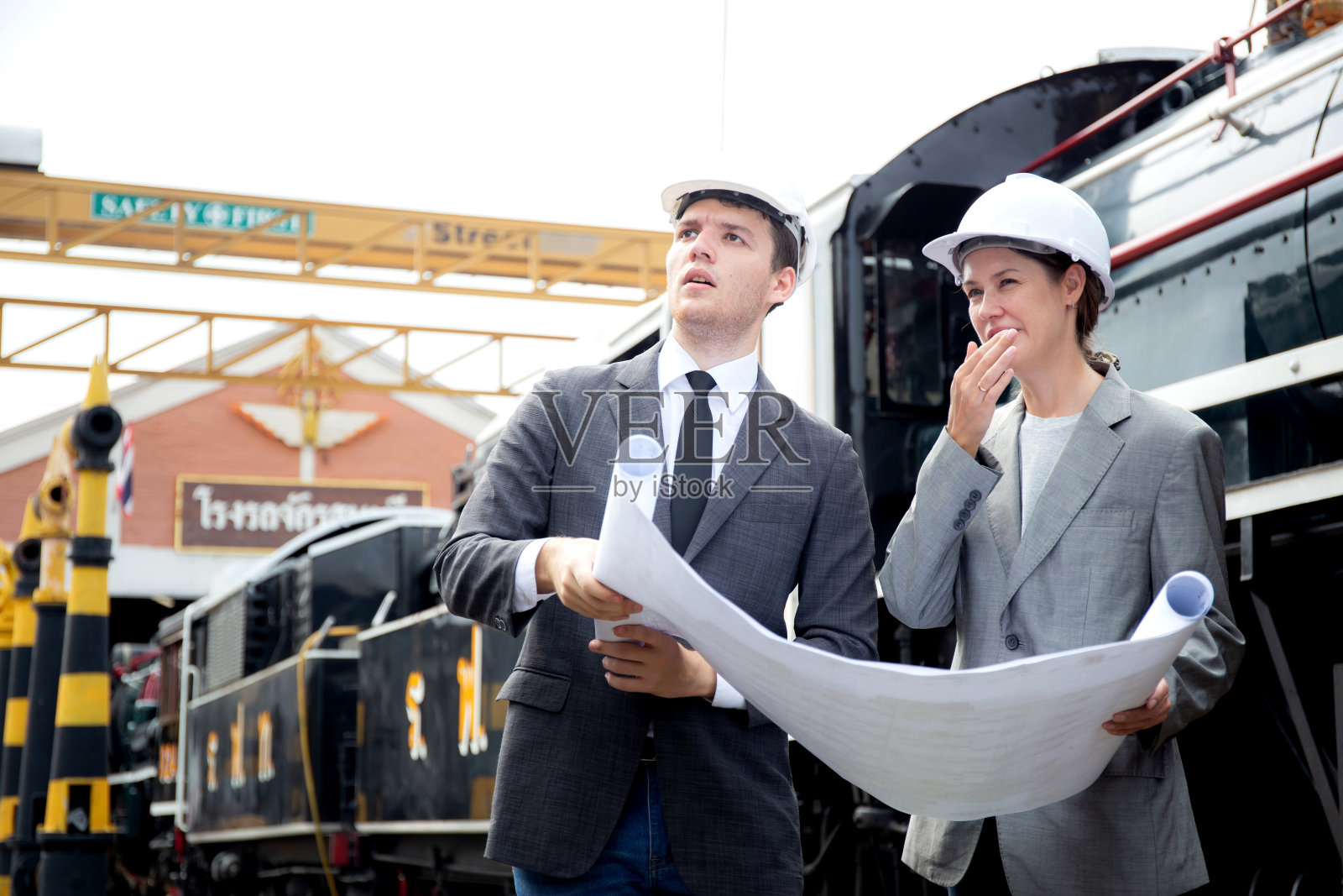 年轻的白人工程师穿着西装在车站检查火车看蓝图，团队工程师检查系统运输，技师检查基础设施、交通和工业。照片摄影图片