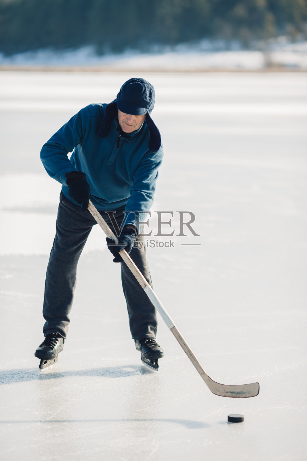 一位老人在冬天结冰的湖面上练习用曲棍球杆击球照片摄影图片