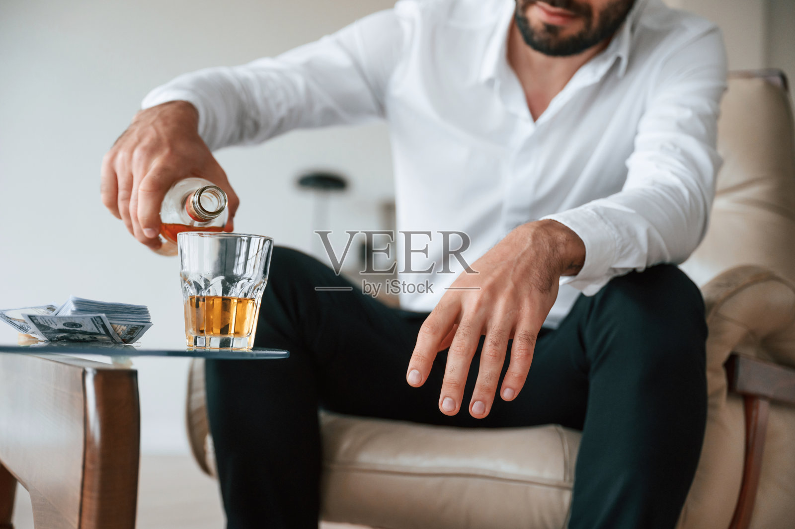 将威士忌倒入玻璃杯中，沮丧的年轻男人在室内酗酒照片摄影图片