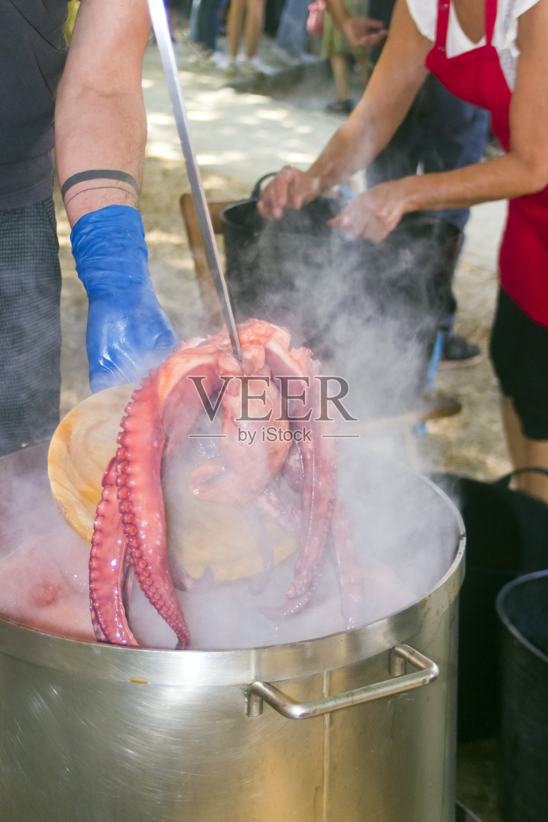 从大锅中取出煮熟的章鱼。照片摄影图片