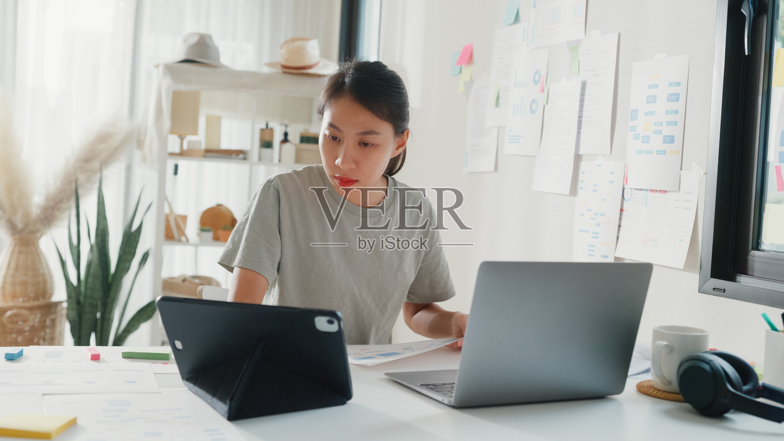 年轻的女孩IT开发程序员在键盘上打字编码编程，在笔记本电脑屏幕上固定数据代码，遵循平板电脑上的代码计划和桌子上的文书工作。照片摄影图片