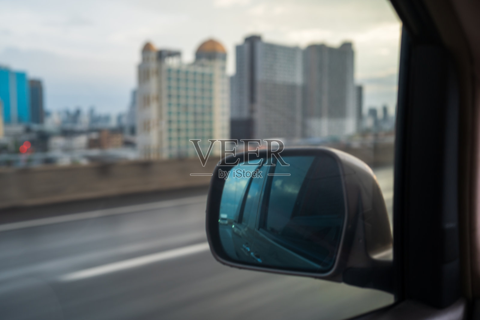 从汽车后视镜看，天空与高速公路上的建筑物。照片摄影图片