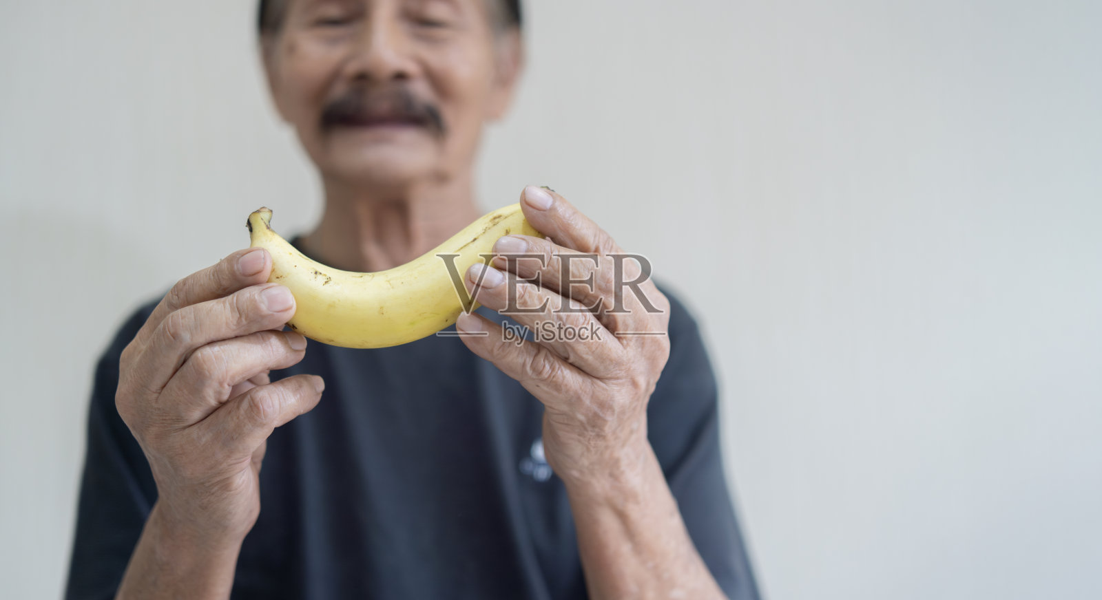 一个留着灰胡子、穿着黑衬衫、在白色背景上显得很孤独的开朗的老人，手里拿着一根香蕉照片摄影图片