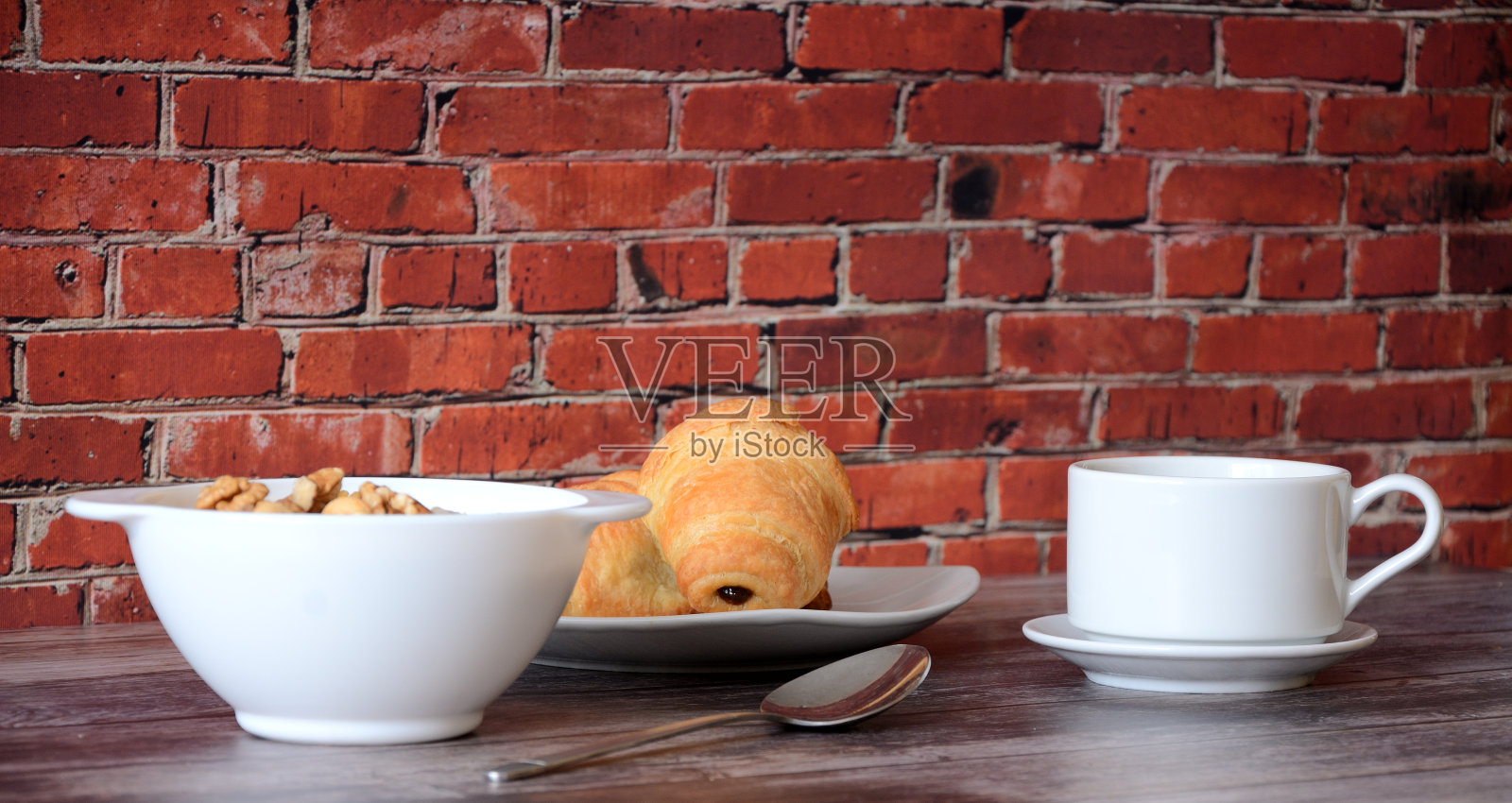 一盘新鲜的坚果燕麦片，两个新鲜的牛角面包和一杯热黑咖啡，放在木桌上。照片摄影图片