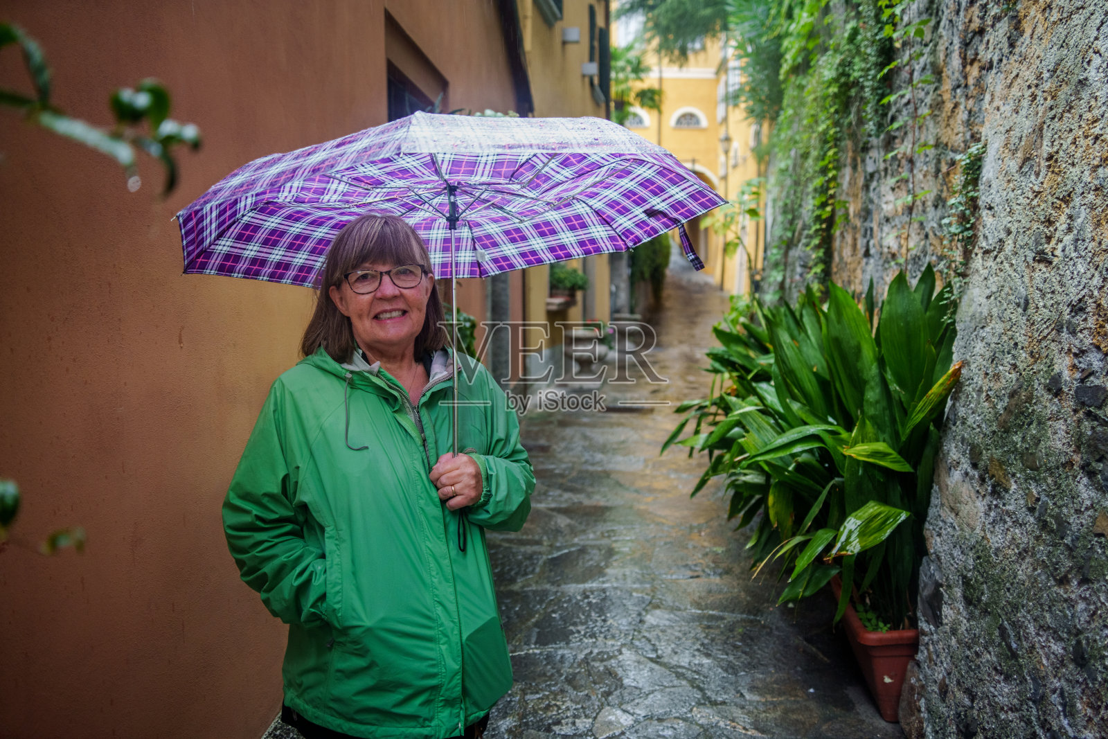 60岁的妇女带着彩色雨伞走在意大利伦巴第湖科莫地区瓦雷纳旅游小镇的鹅卵石街道上照片摄影图片