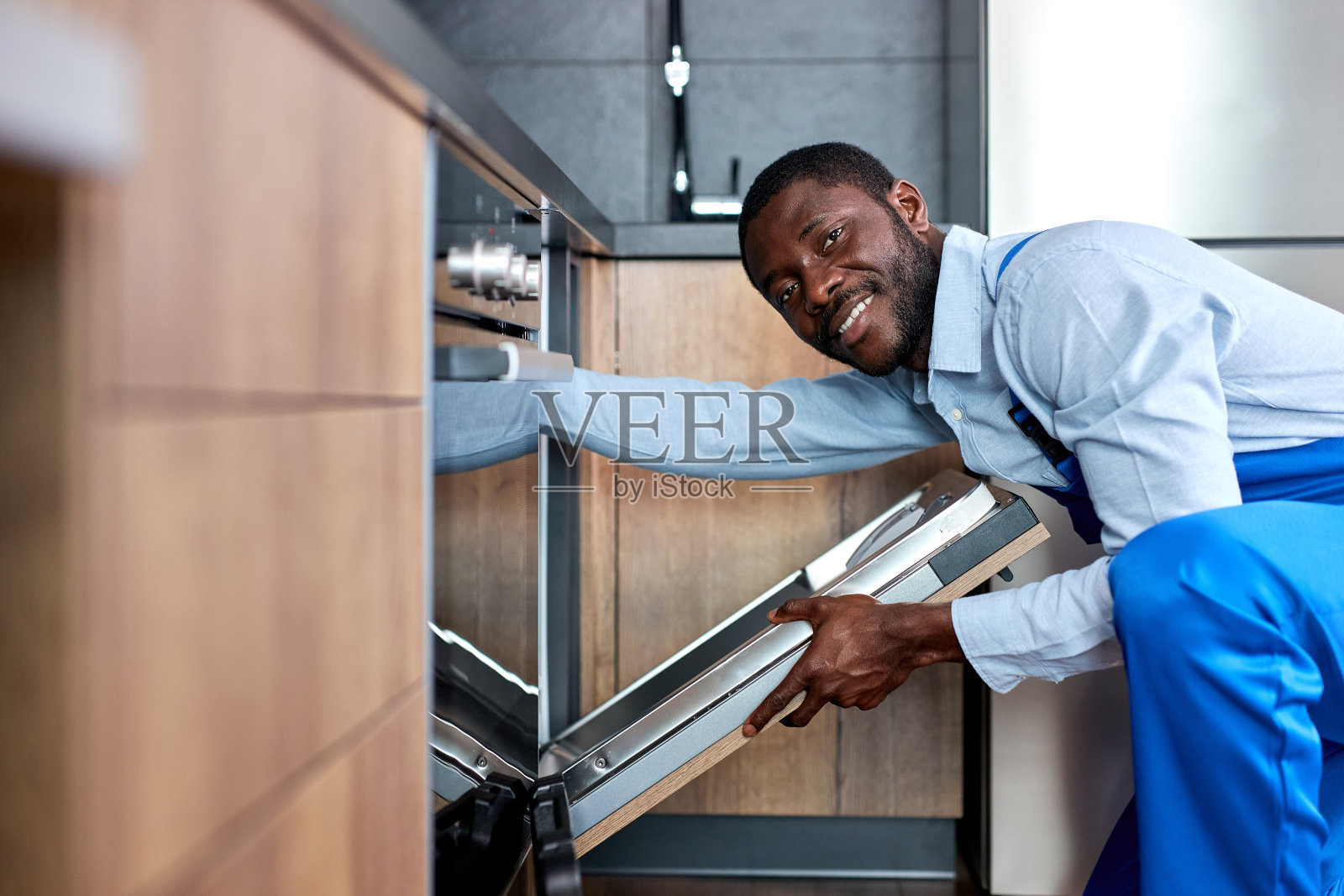 穿着蓝色工作服、面带微笑的非洲勤杂工要去修理洗碗机照片摄影图片