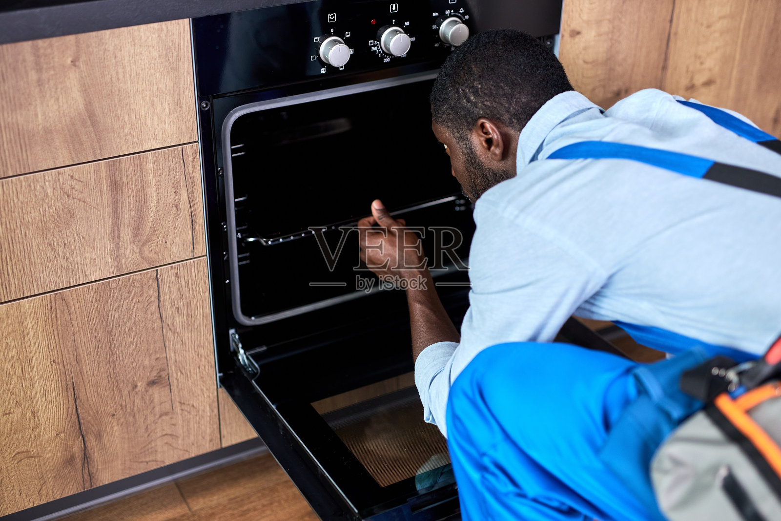 年轻的非洲勤杂工在家检查厨房里的电烤箱。设备维修照片摄影图片
