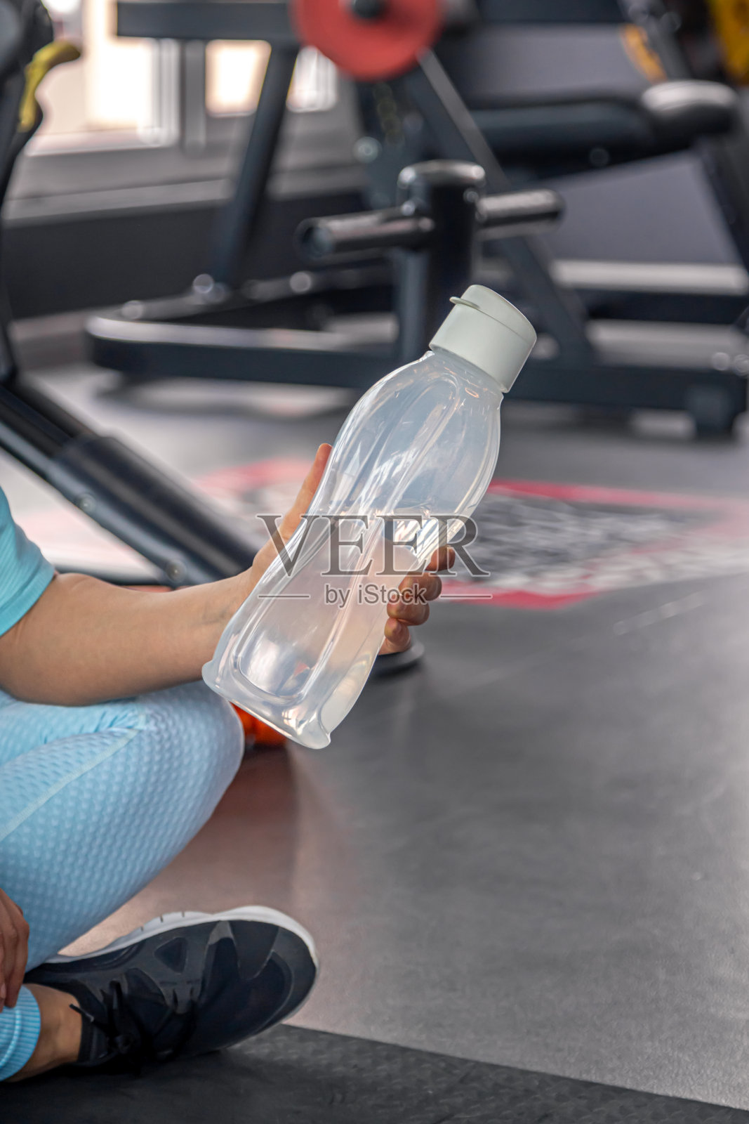 一位女士在健身房里拿着一瓶水。照片摄影图片