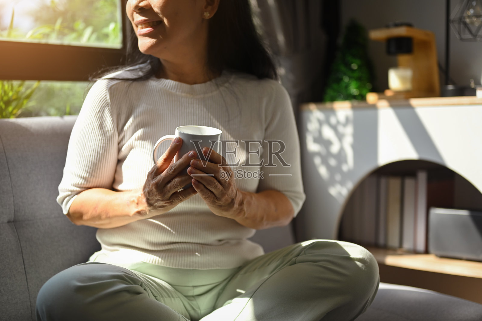 一位无忧无虑的60多岁中年女士，喝着热饮，悠闲地躺在沙发上，望着窗外照片摄影图片