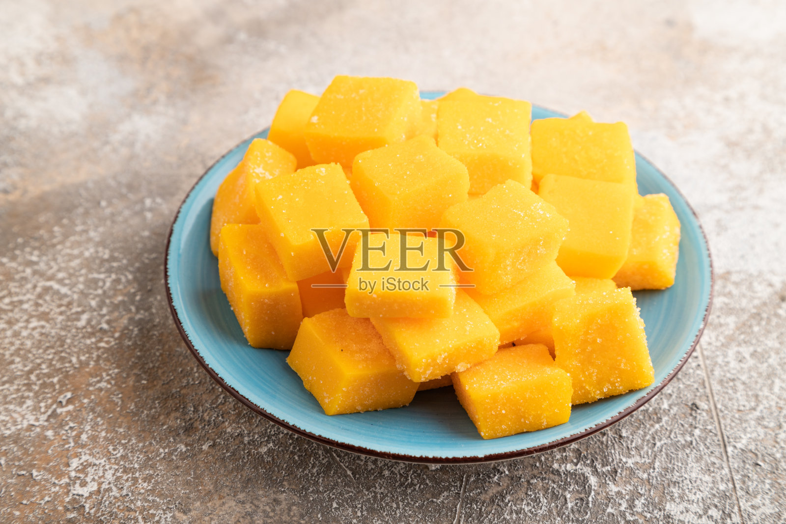 干芒果块放在棕色混凝土上的蓝色盘子上，侧视图。照片摄影图片