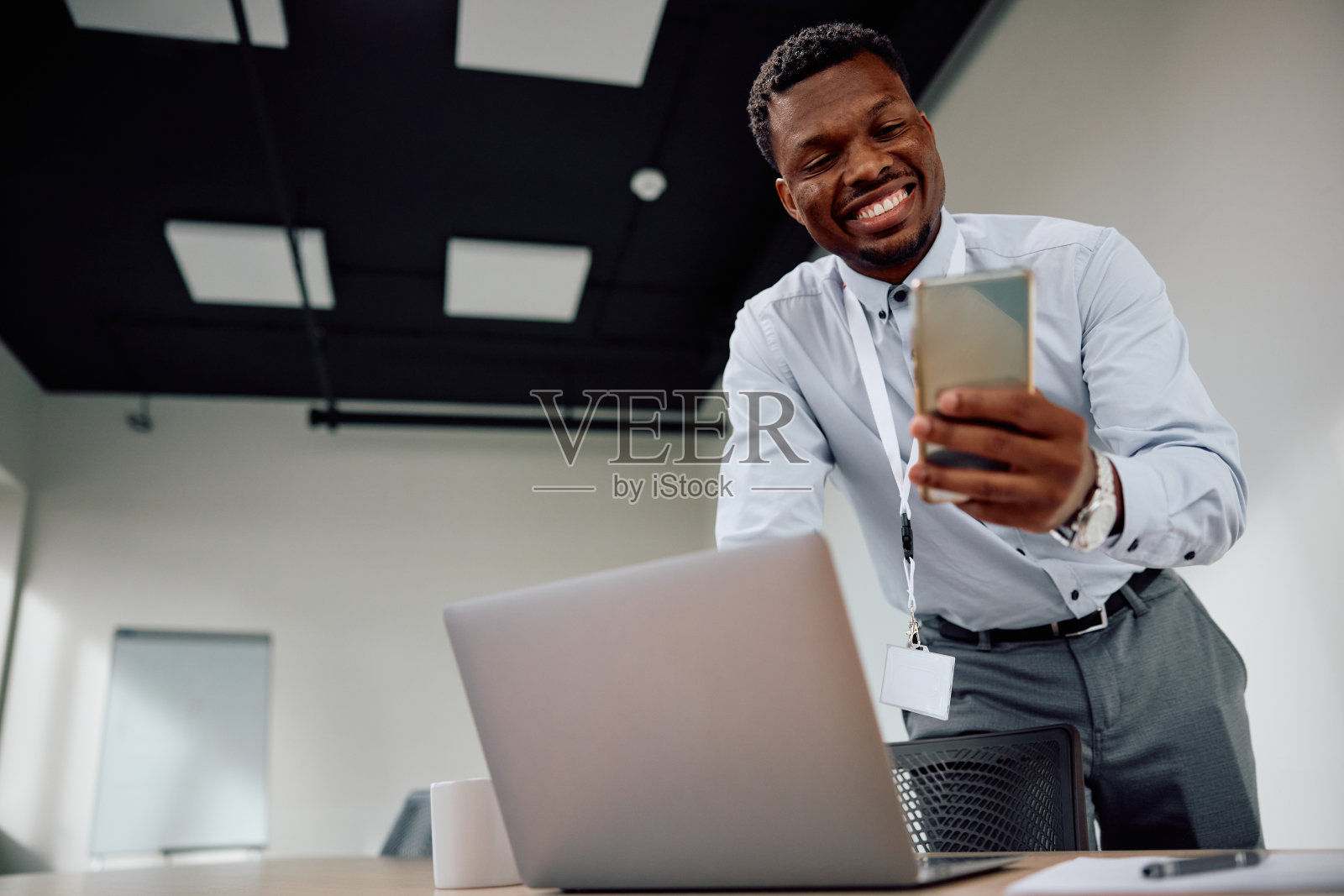 快乐的黑人商人一边在办公室工作一边发短信。照片摄影图片