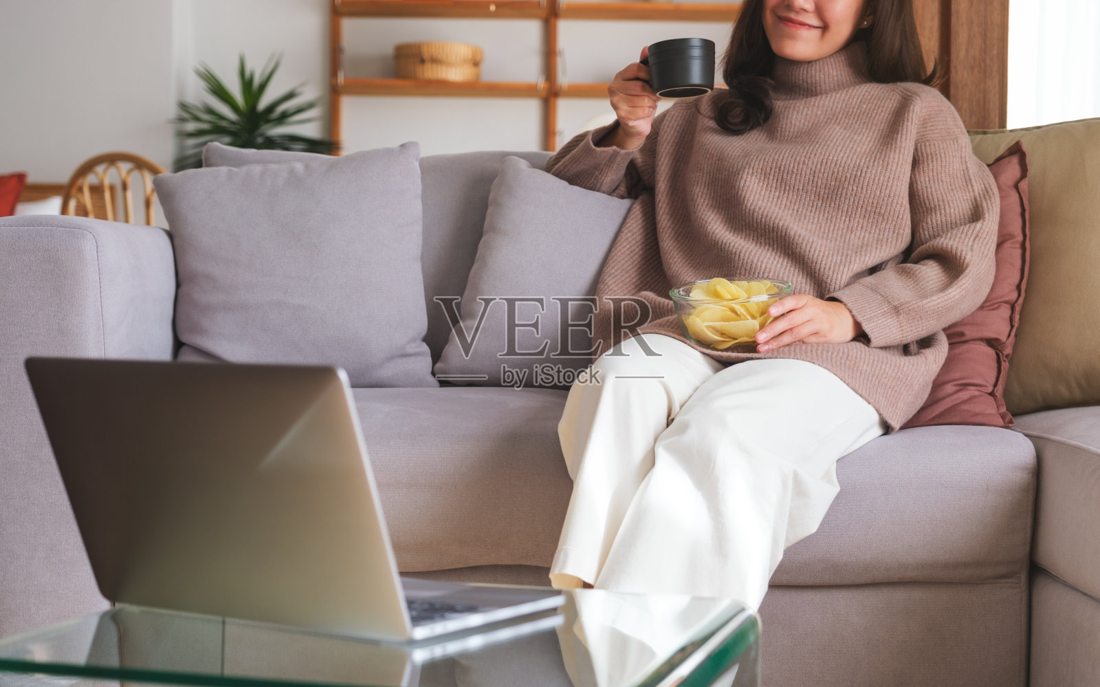 一个年轻女子在家里边看笔记本电脑边喝酒吃零食的特写照片摄影图片