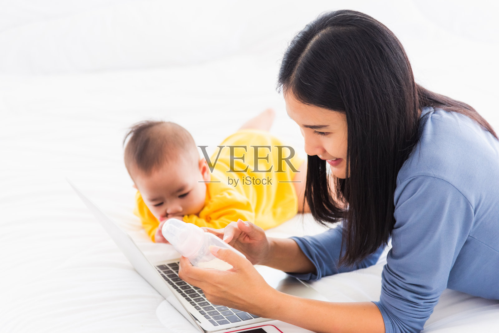 亚洲年轻漂亮的新妈妈在家里的卧室里用笔记本电脑查找和阅读牛奶混合瓶的信息照片摄影图片