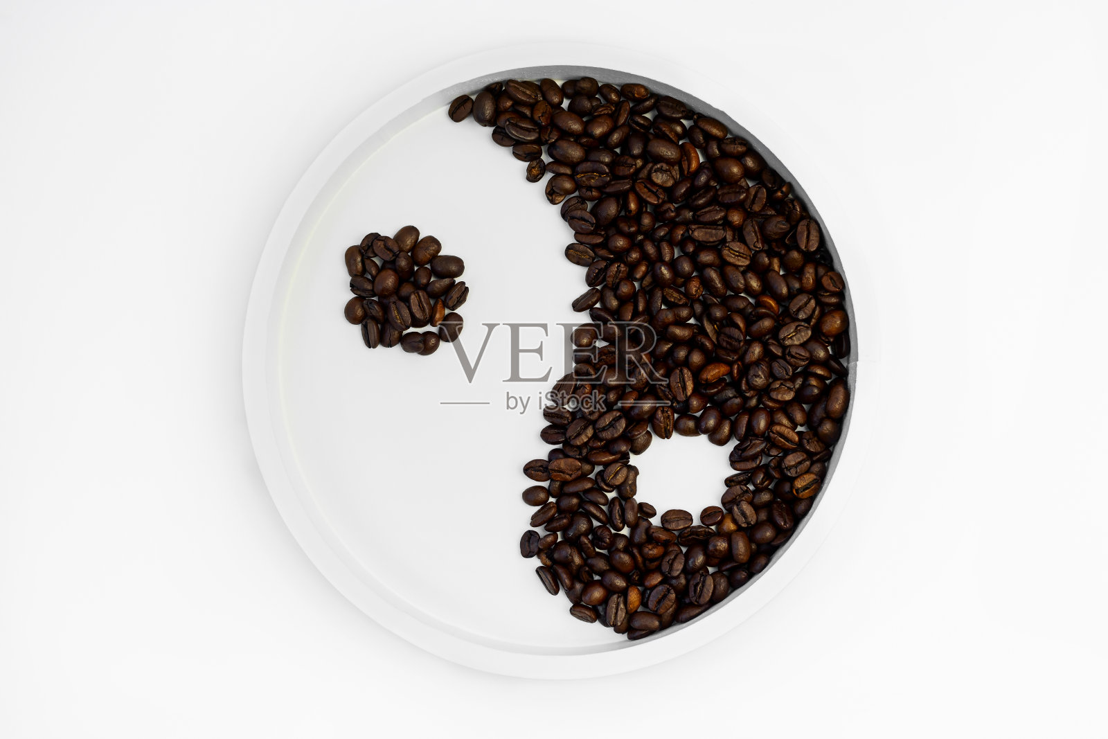 烤好的咖啡豆散落在一个圆形的白色支架上，形成一个阴阳的象征。照片摄影图片