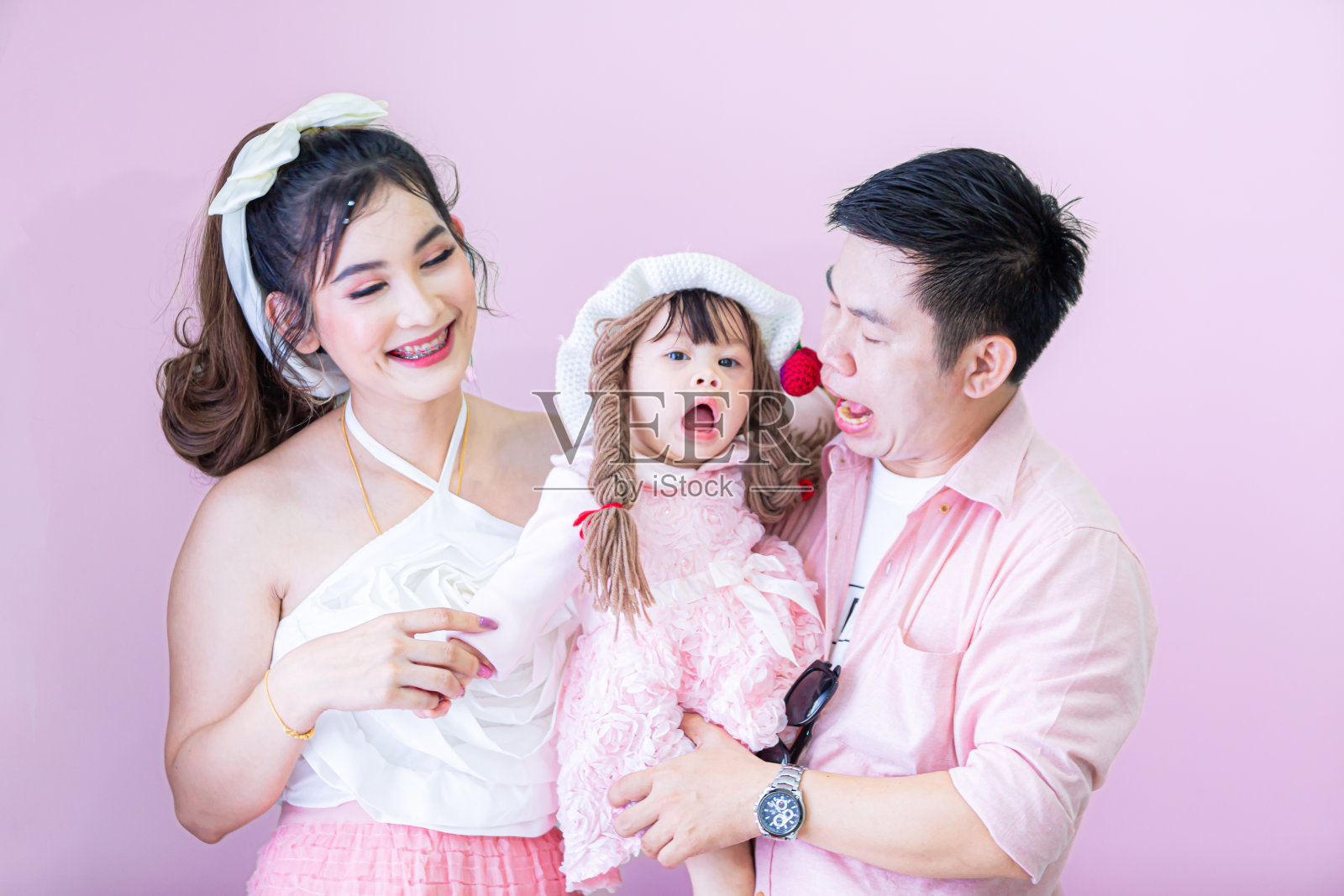 父亲，母亲和女儿的全家福，幸福的亚洲家庭，全尺寸，快乐地微笑，父母，父亲和女儿，十几岁的女儿穿着蓝色的衣服看着相机，彼此拥抱，孤立在普通的柔和的浅粉色背景照片摄影图片
