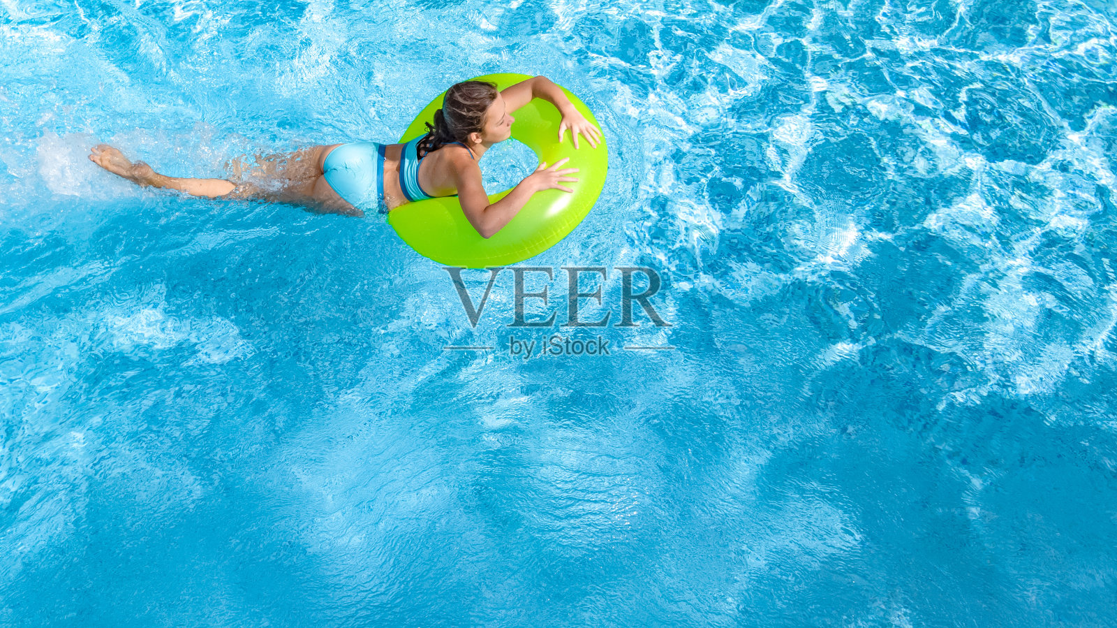 活跃的年轻女孩在游泳池空中俯瞰从上面看，青少年放松和游泳的充气环甜甜圈，并在水中享受乐趣的家庭度假，热带度假胜地照片摄影图片