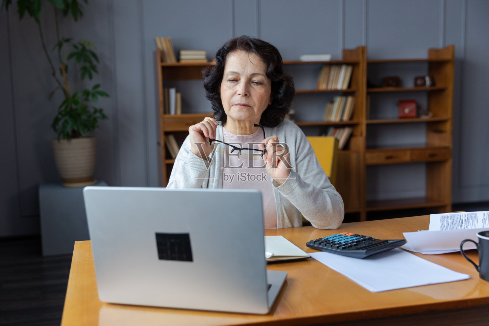 自信时尚的欧洲中年女性在家里使用笔记本电脑。时尚的大龄60多岁的女士坐在桌子前看着电脑屏幕打字聊天阅读写电子邮件。照片摄影图片