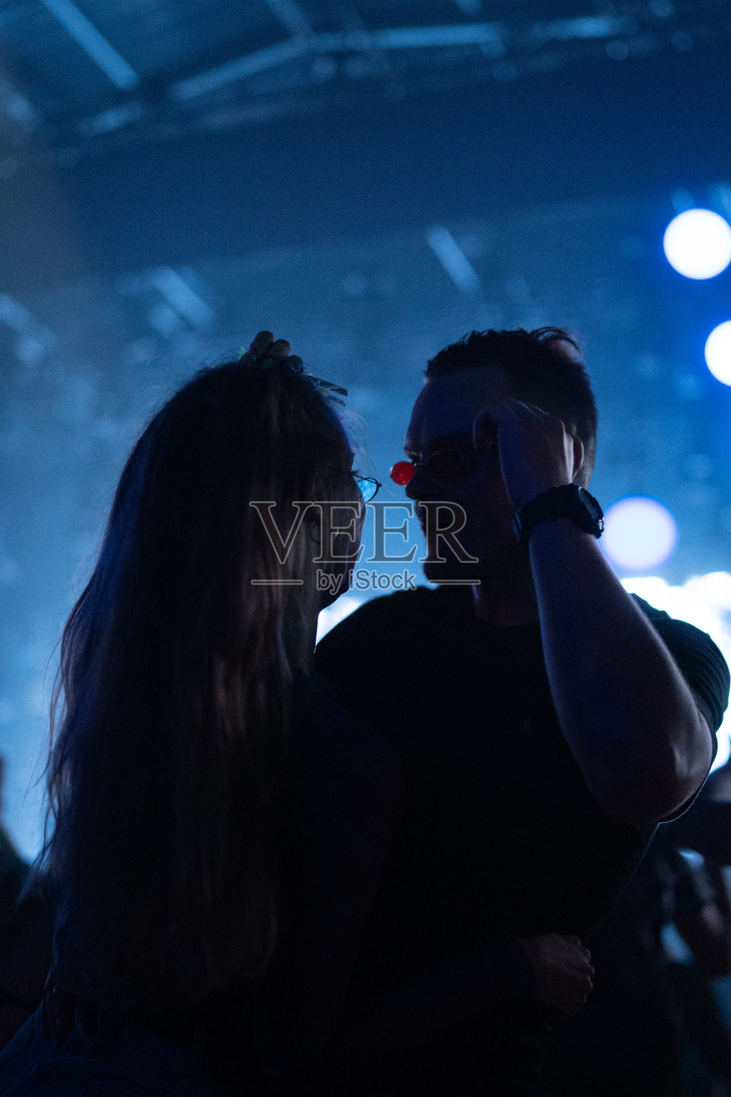 观看音乐表演的一群人。朋克浪漫的情侣一起跳舞。被舞台上的蓝色灯光照亮照片摄影图片