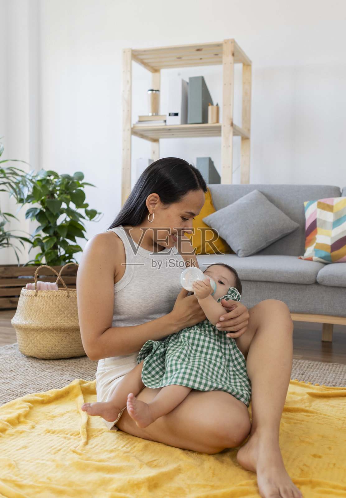 快乐的拉丁母亲坐在她房子的地板上给她的孩子一个奶瓶照片摄影图片