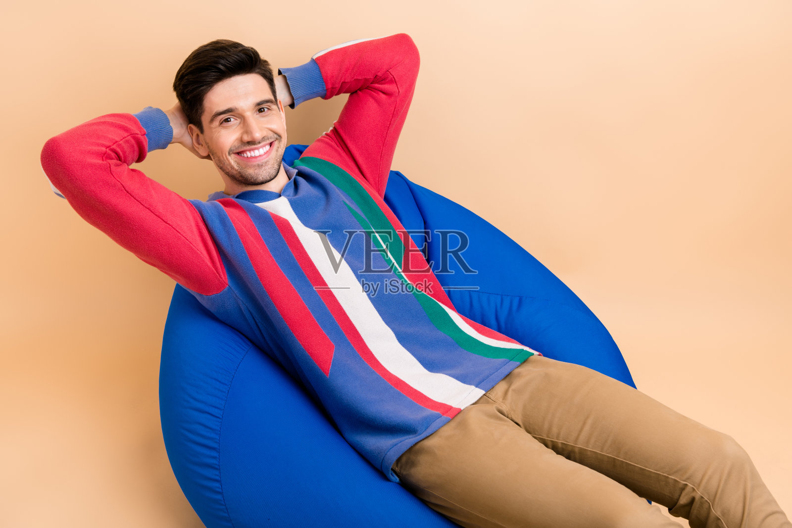 在米色的背景下，辛苦工作后，年轻人坐在舒适的豆包里，微笑着小睡照片摄影图片