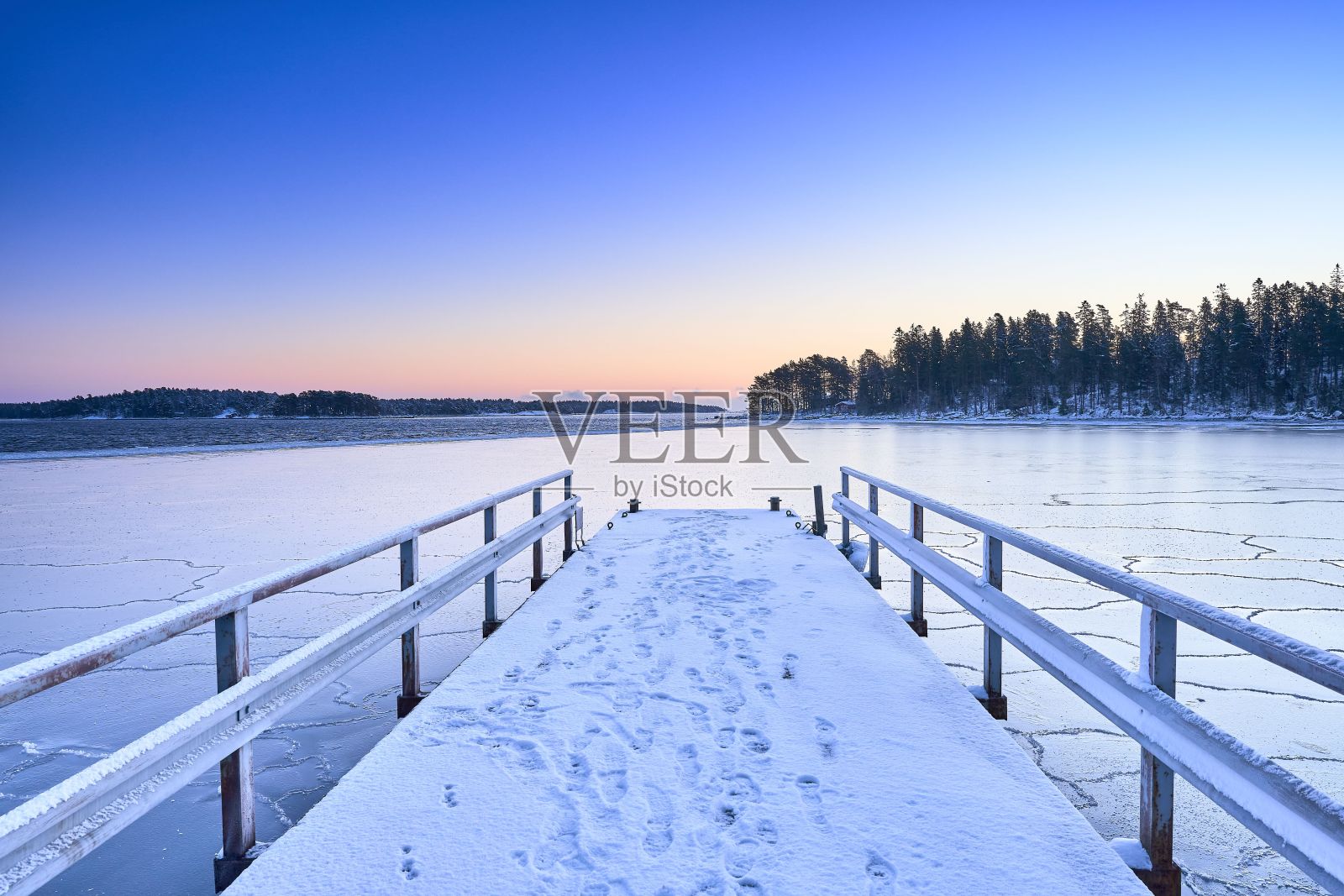 白雪覆盖的木制码头延伸到一个原始的，冰冻的湖泊。照片摄影图片