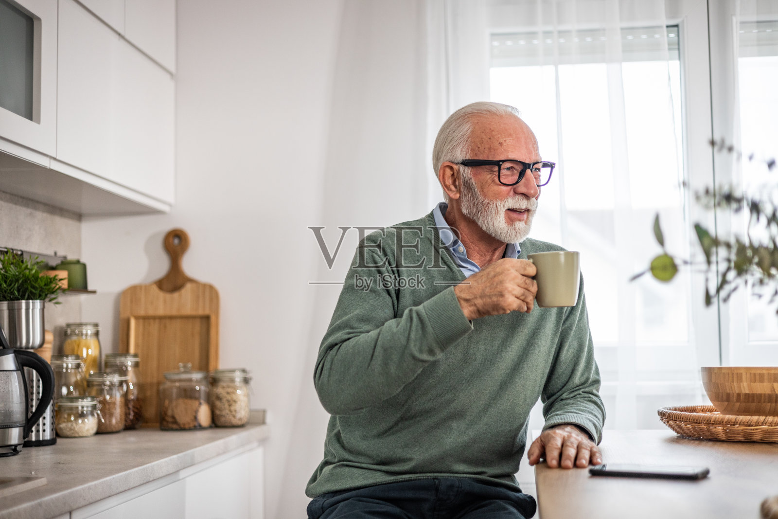 老人，领养老金的人，坐在厨房里开心地笑着，喝着热咖啡或茶，早晨的例行程序，无忧无虑的退休日子照片摄影图片