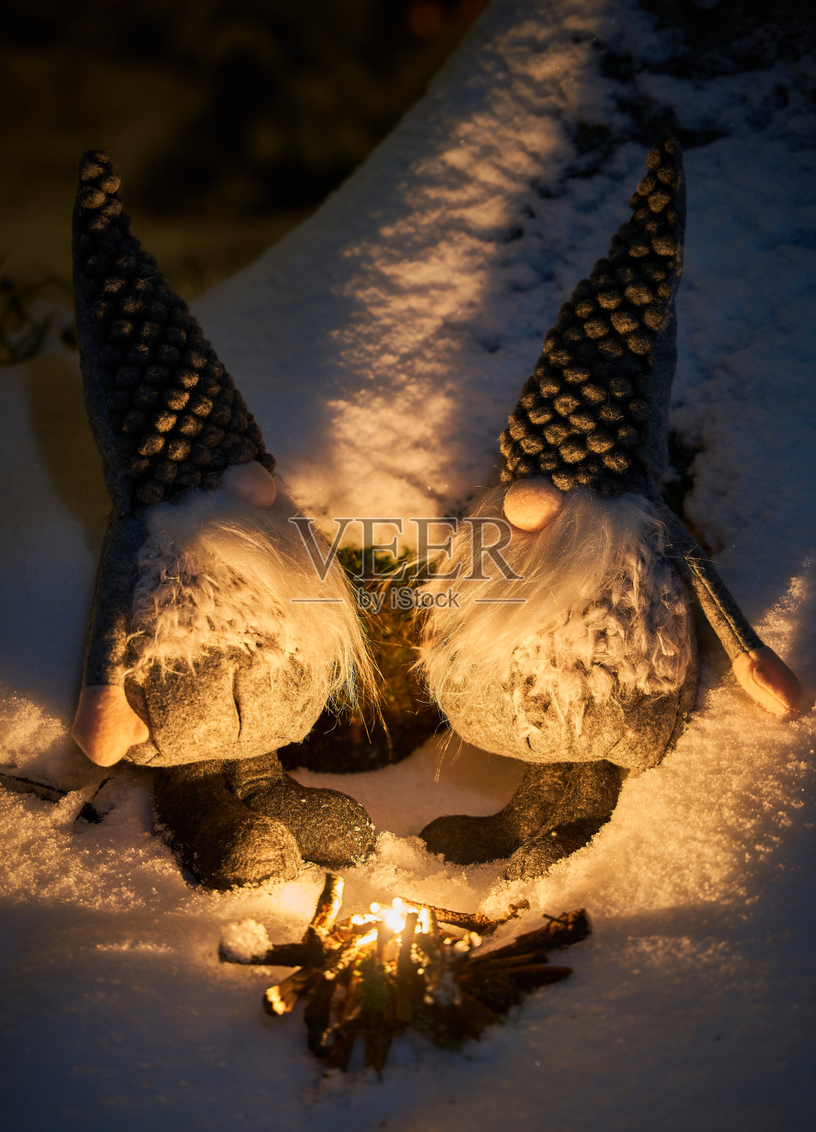 可爱而欢快的侏儒坐在雪地里，被点燃的蜡烛的温暖光芒照亮。照片摄影图片