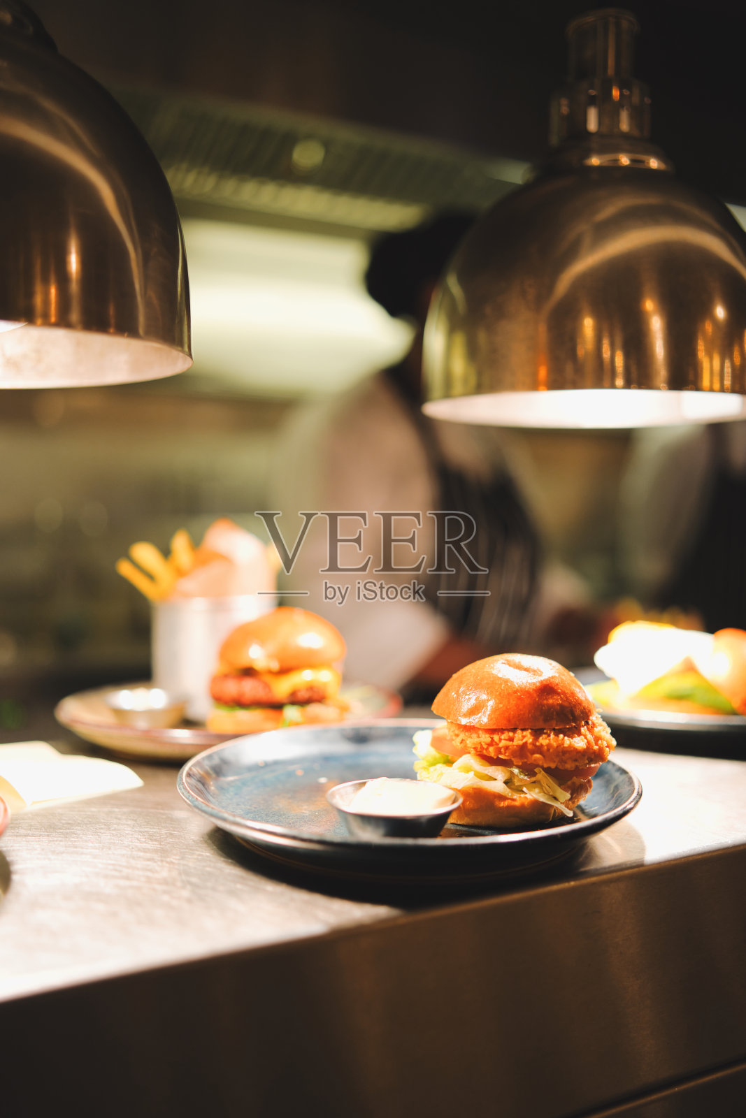 餐厅吧台上的面糊鸡肉汉堡。背景是厨房。照片摄影图片