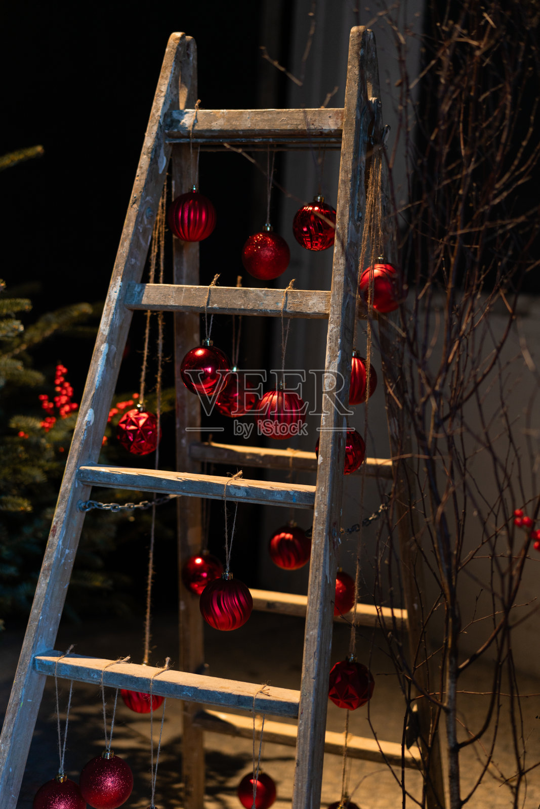 车间谷仓的旧梯子上挂着红球的圣诞装饰。照片摄影图片