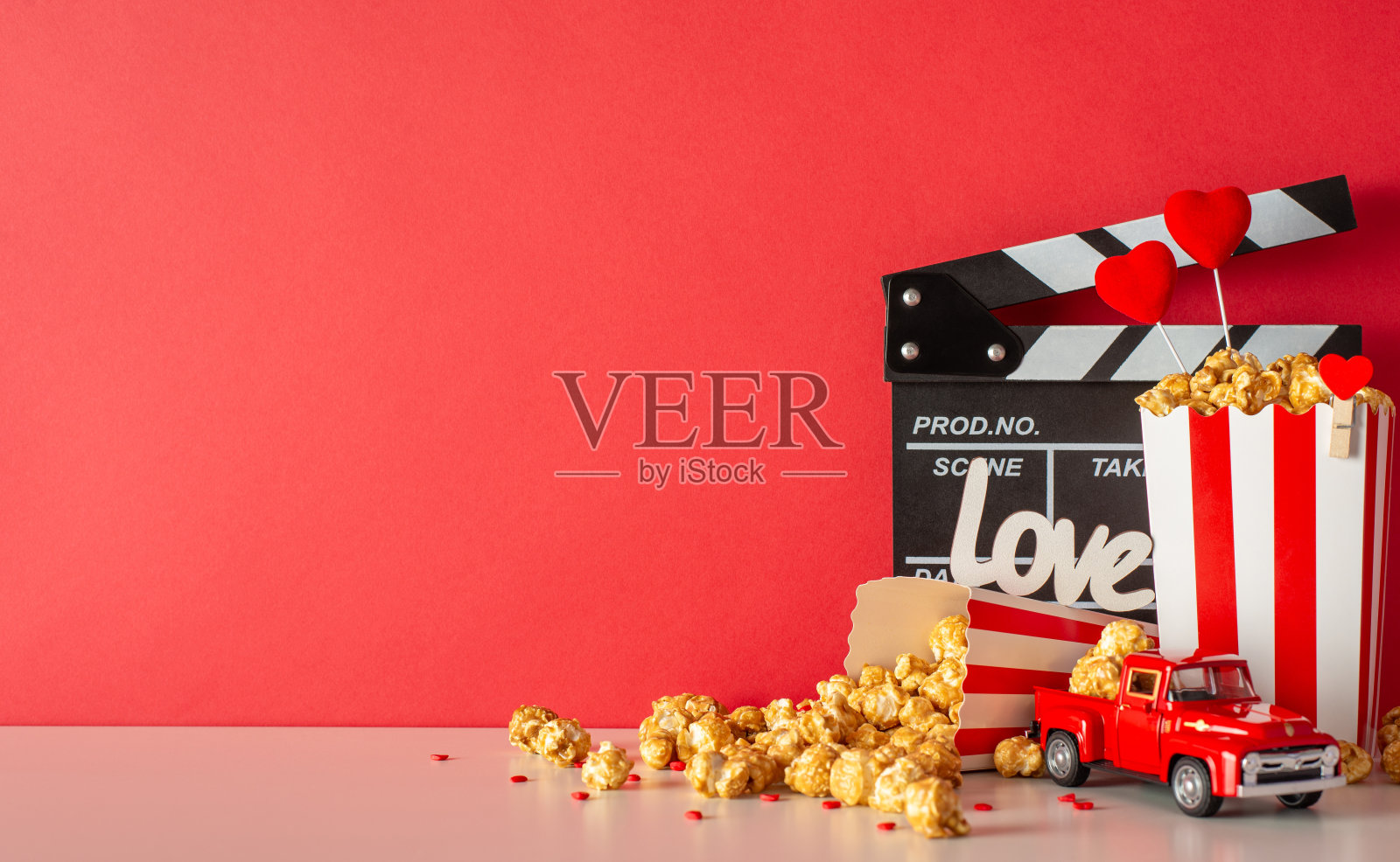 情人节剧首映。一张桌子的侧视图，桌子上有隔板、微型送货车、条纹爆米花盒和红色墙壁上的心形装饰。拥抱充满爱的氛围照片摄影图片