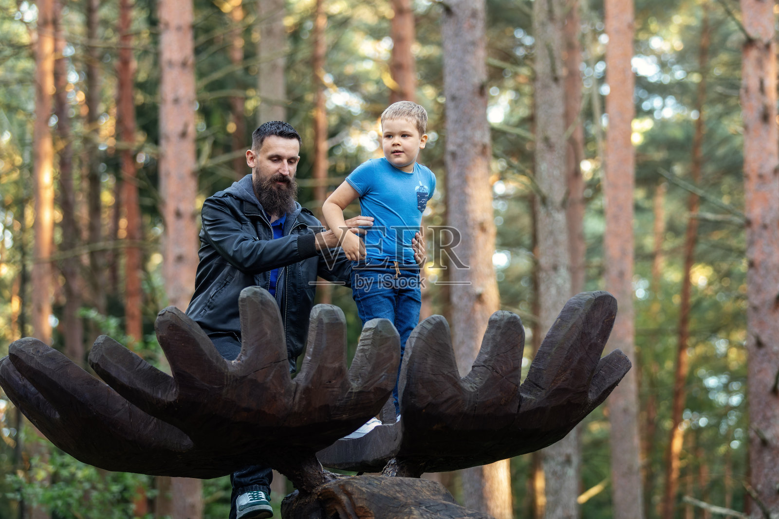 父子在森林里的大木鹿角上的低角度肖像。父亲紧紧地抱着他的孩子，以免他摔倒照片摄影图片