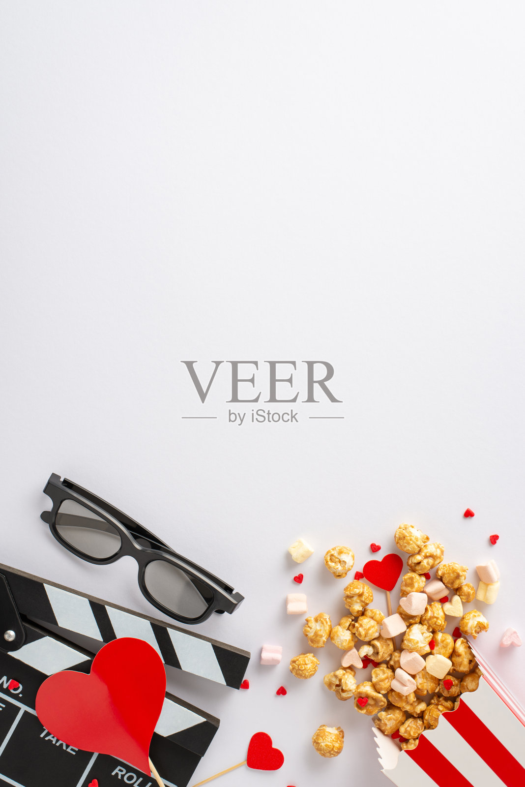 情人节看充满爱情的电影。垂直顶视图隔板，3D眼镜，条纹爆米花盒与心脏装饰，棉花糖，和撒糖。白色背景，留出文字或广告的空间照片摄影图片