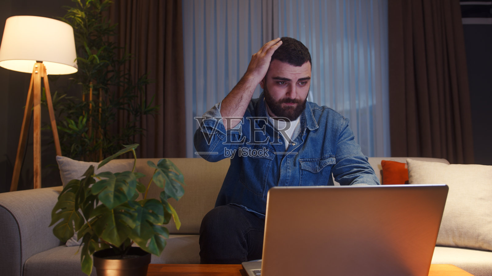 年轻男子在家中坐在沙发上使用笔记本电脑，感到焦虑和压力照片摄影图片