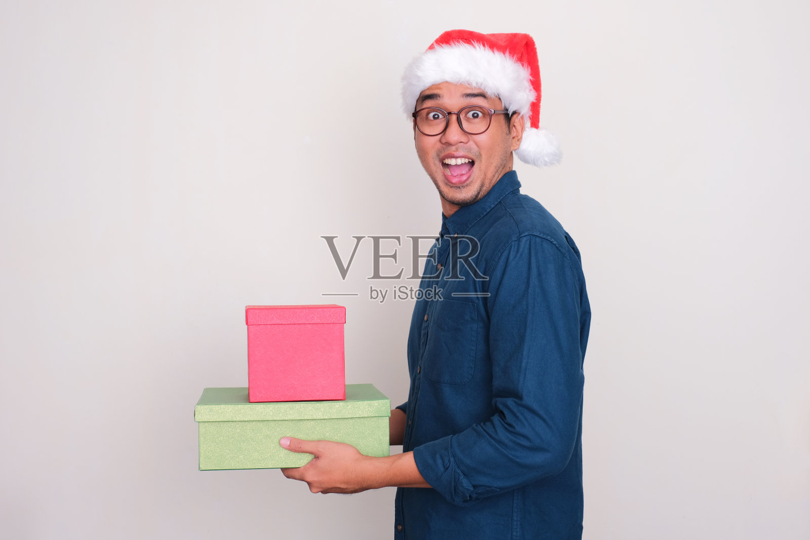 一个戴着圣诞帽的男人拿着礼品盒，脸上露出惊讶的表情照片摄影图片