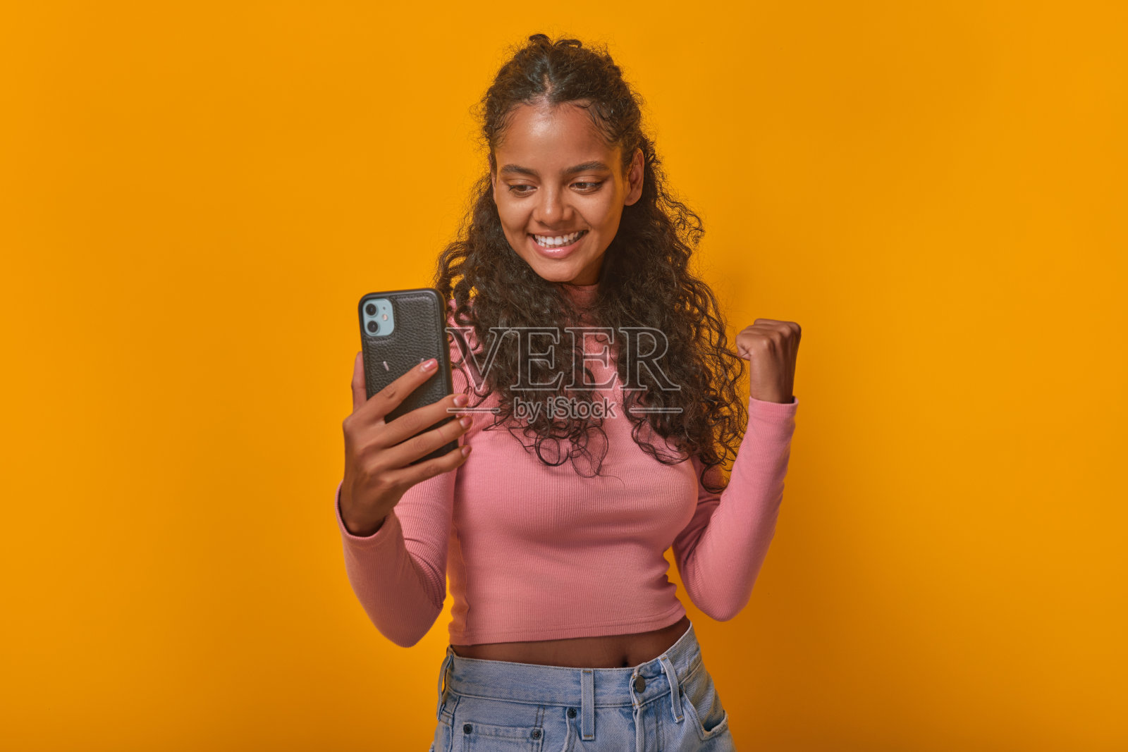 年轻的印度女子拿着手机，在演播室里做着胜利的手势照片摄影图片