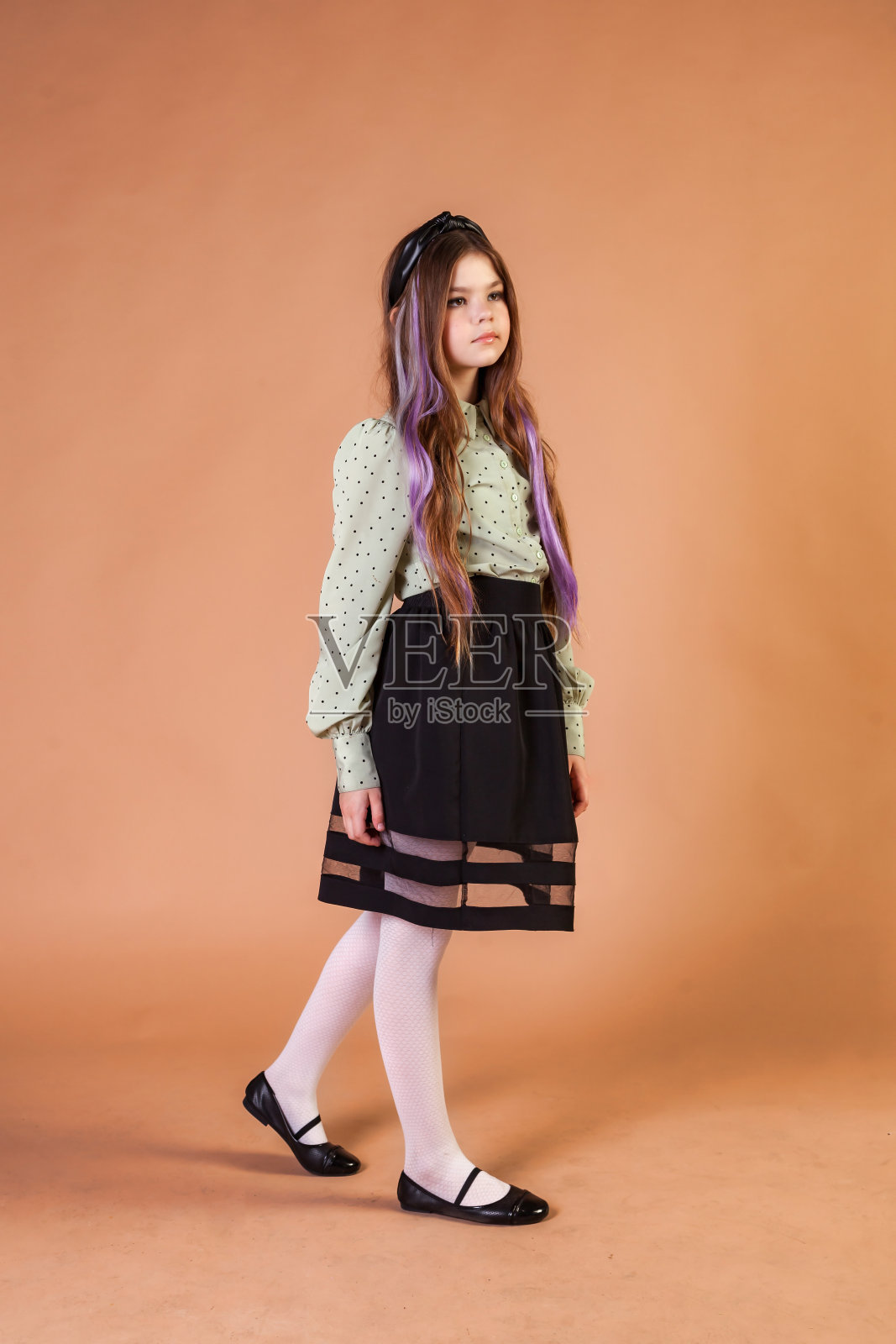 工作室拍摄的10岁时尚女孩模特，在米色背景下沉思的脸，无聊地抬头看向别处。完整长度的时尚青少年封面孩子摆姿势。A代概念。复制广告文本空间照片摄影图片