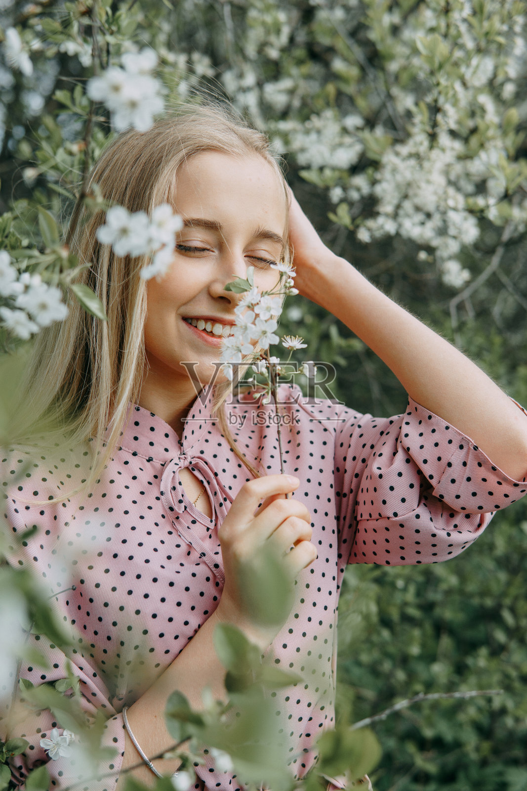 春天，金发女郎在开满樱花的花园里散步。女性肖像，特写。一个穿着粉色圆点连衣裙的女孩。照片摄影图片