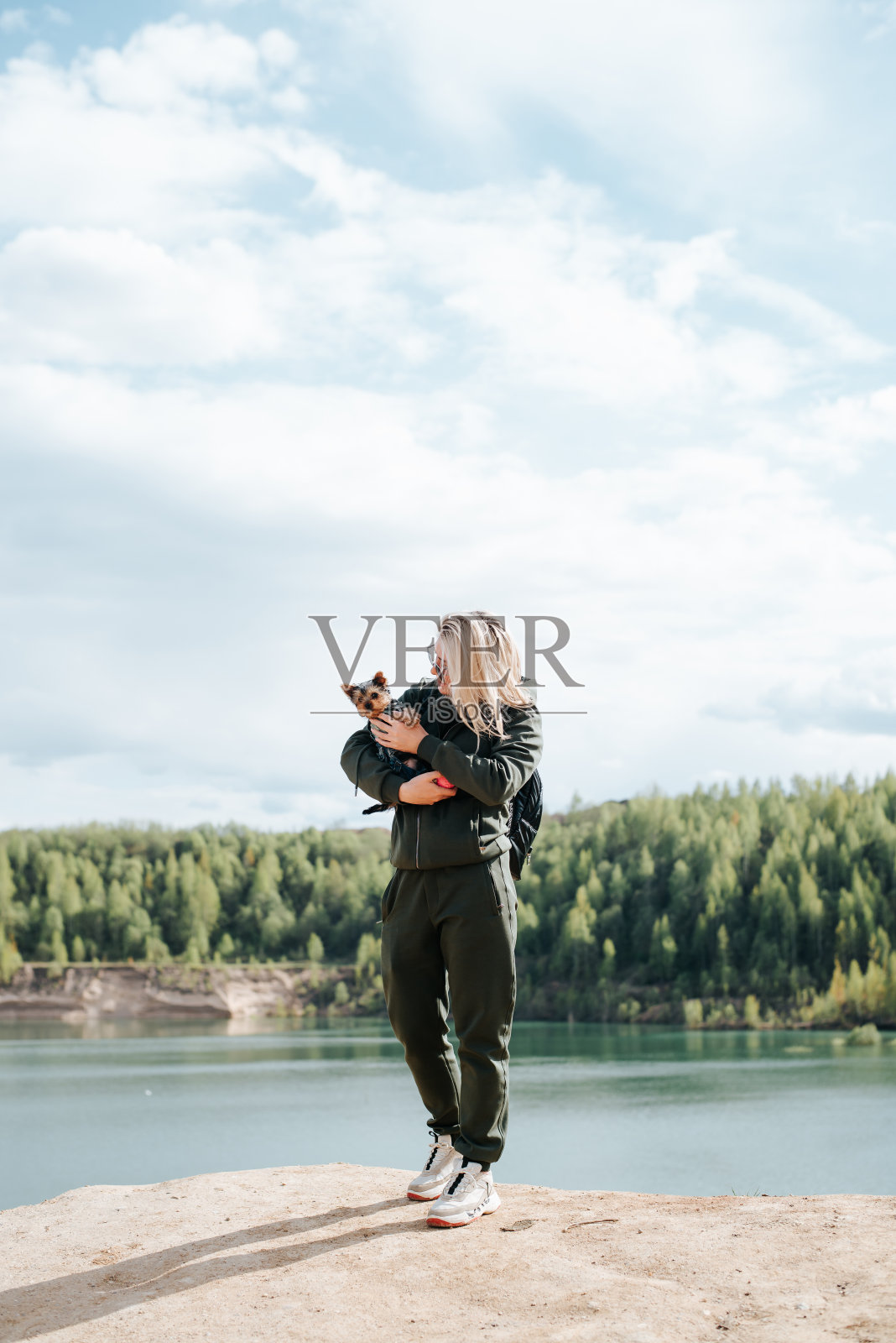 微笑的年轻女子和她的宠物在湖边。垂直的角度照片摄影图片