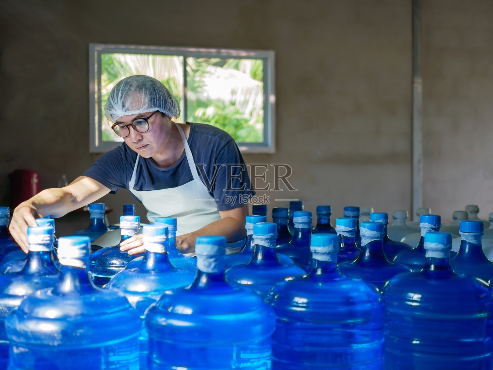 在饮用水工厂检查出厂前蓝色加仑饮用水的亚裔工人或质量检验员。饮用水商，小企业，商店，仓库照片摄影图片