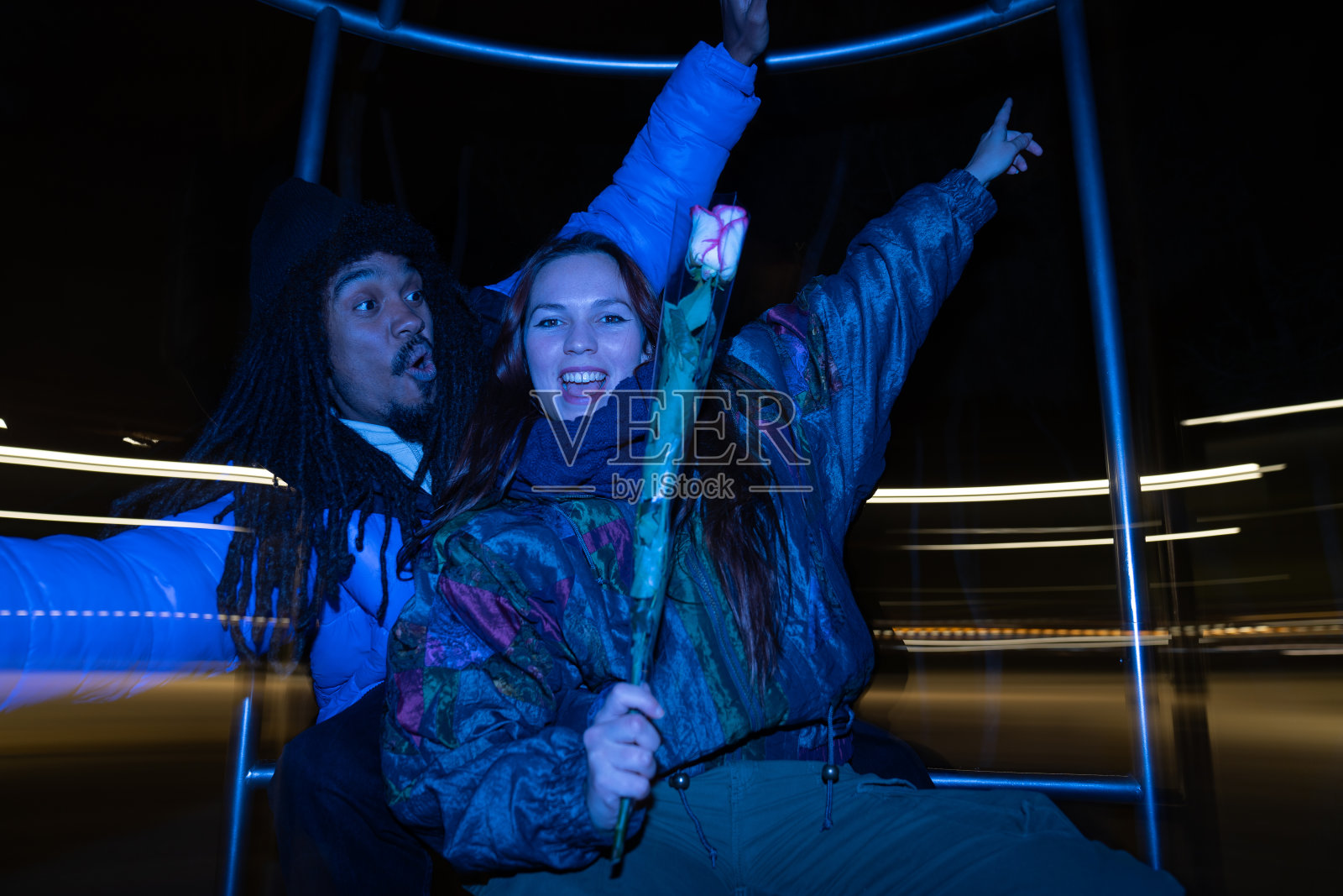 带有闪光灯和蓝光效果的复古摄影。非洲男孩和高加索女孩情人节在街上带着玫瑰约会。照片摄影图片