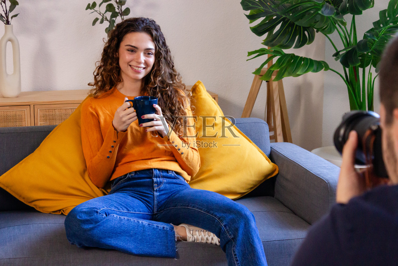 年轻女子坐在沙发上，端着一杯咖啡，看着相机照片摄影图片