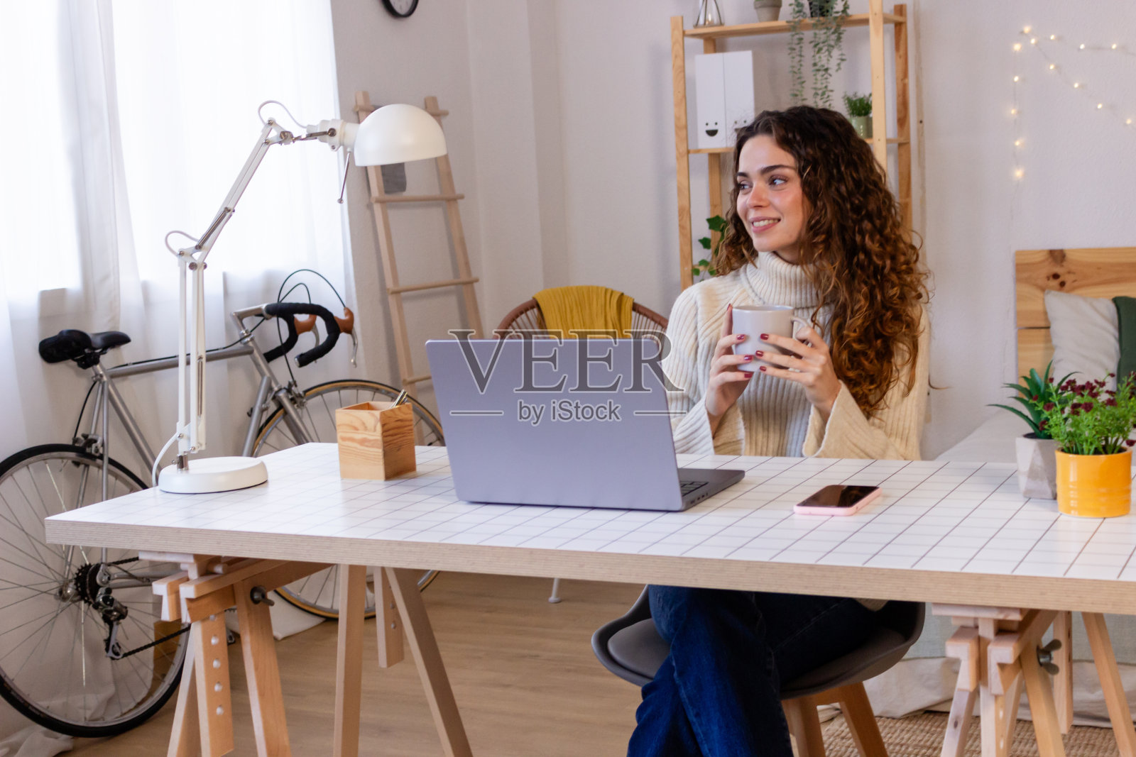 年轻女子坐在桌子旁，拿着笔记本电脑和一杯咖啡。照片摄影图片