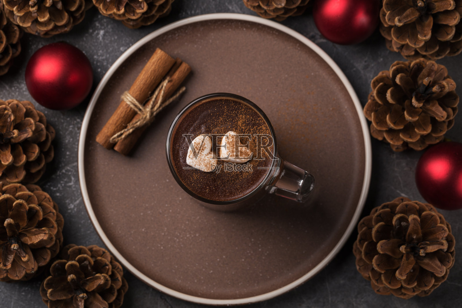 俯视图，一杯热巧克力和棉花糖放在一个黑色的桌子上。圣诞和新年用红色圣诞球、松果、肉桂棒组成。照片摄影图片