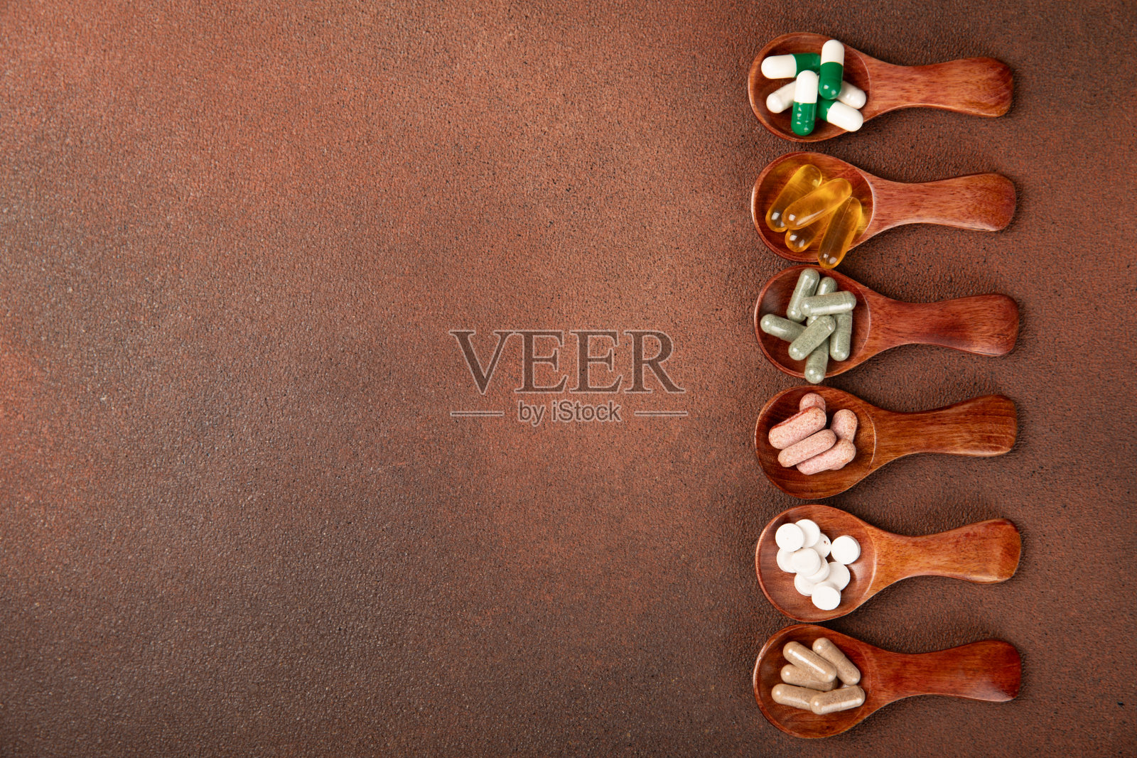维生素和补品。多种维生素片在木勺纹理背景。多吃新鲜健康的水果。食品补充剂。平的。文本空间。本空间照片摄影图片
