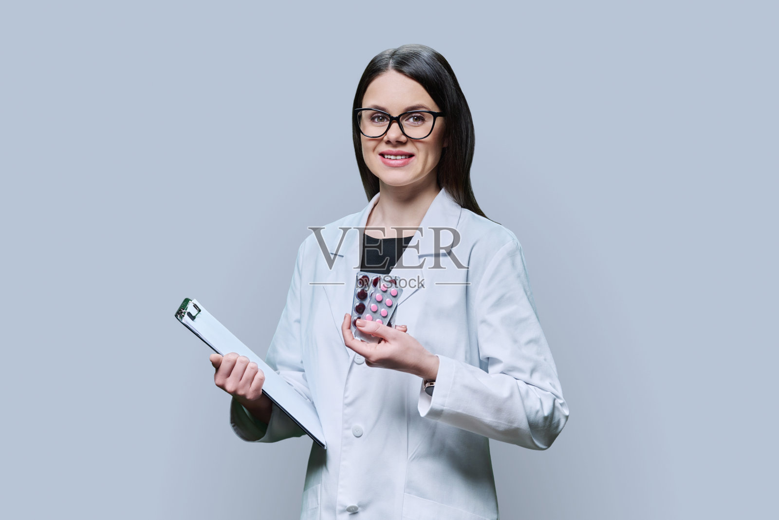 年轻的女医生在灰色背景上展示药片照片摄影图片