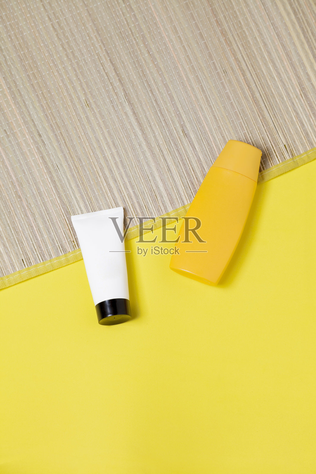 黄色背景上的草席上放着几瓶防晒霜照片摄影图片