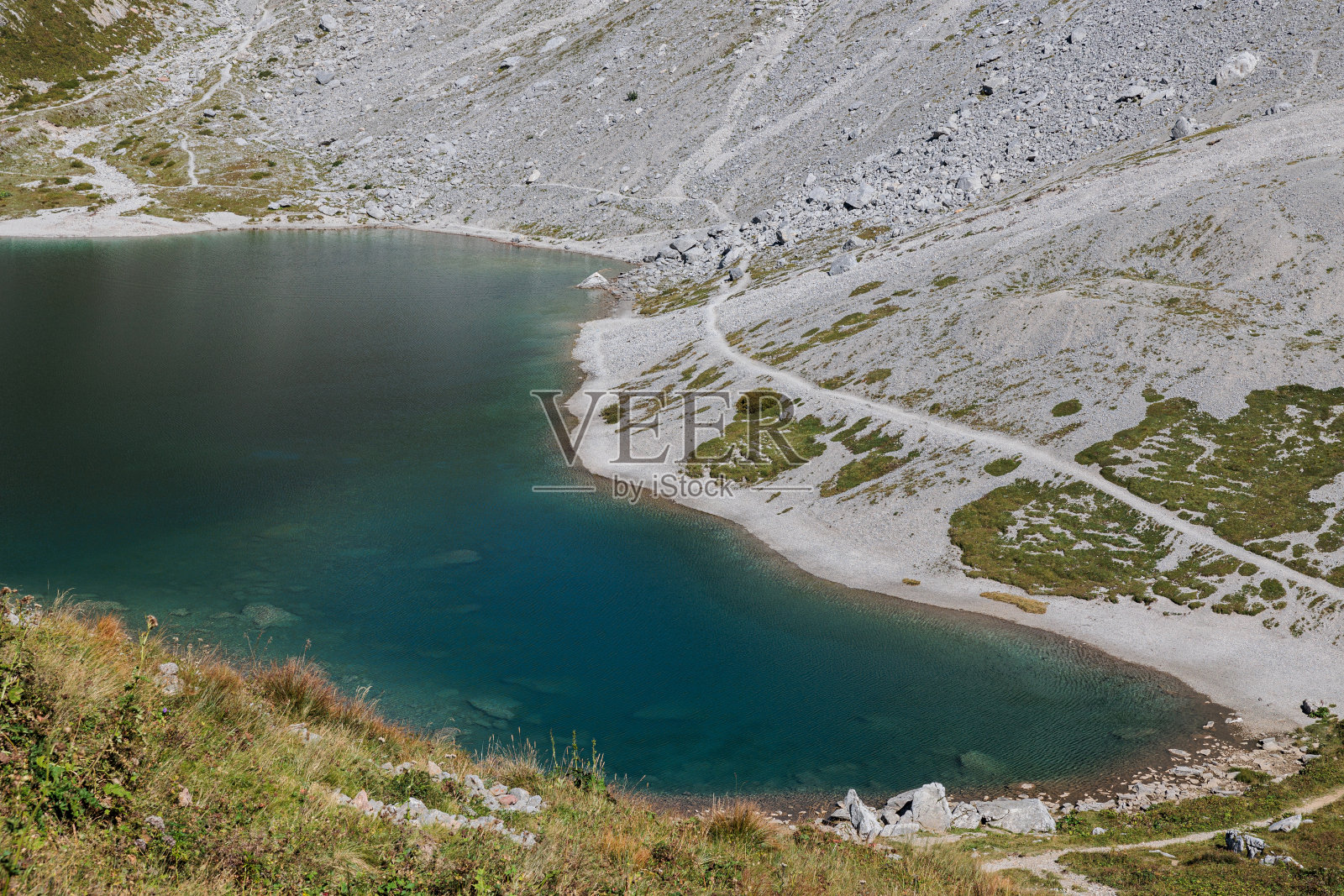 从上方近距离观察沃拉亚湖深蓝色和绿色的湖水，周围是长满草和岩石的斜坡，秋天早晨的阳光照亮了湖水照片摄影图片