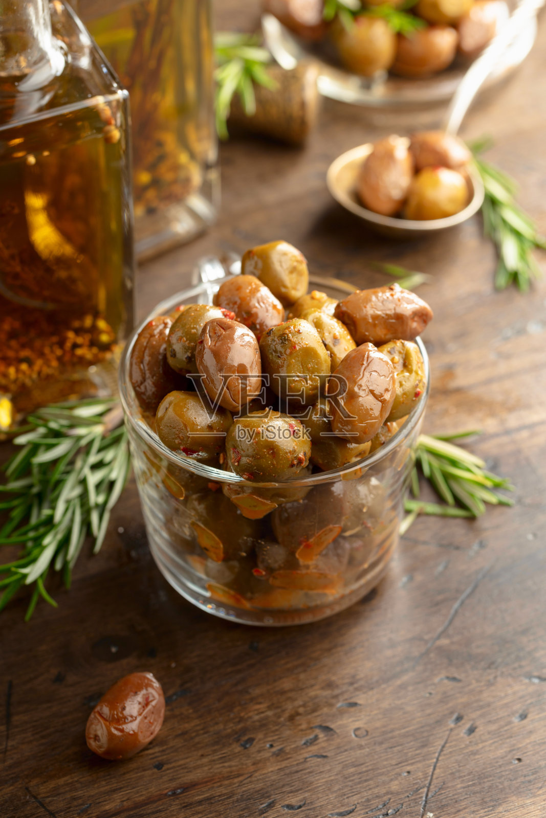 木桌上放着辣橄榄和几瓶橄榄油。照片摄影图片